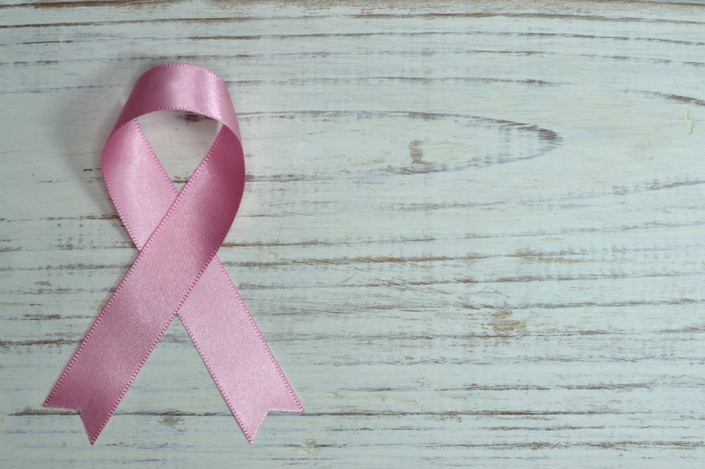 Rosa Schleife als Symbol für Krebserkrankungen vor Holzhintergrund