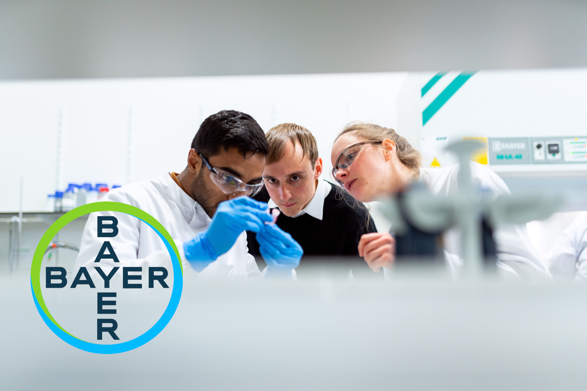 Drei Personen bei der Laborarbeit - Logo von Bayer